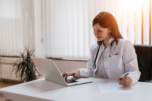 Attractive female doctor working on her laptop in her office