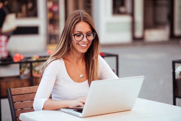 Attractive female freelancer working on laptop in the cafe outdoors.