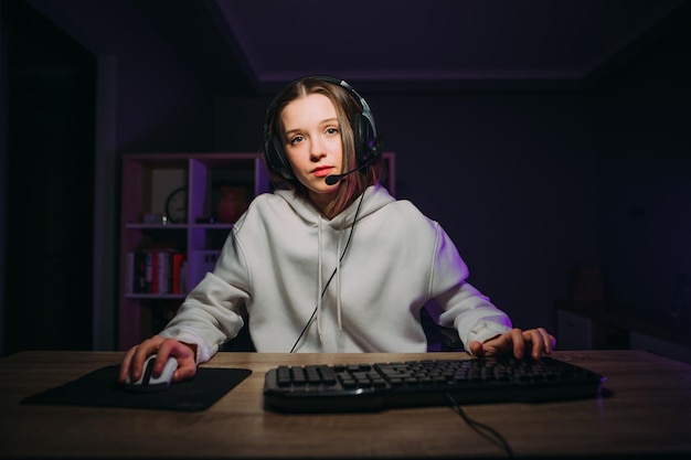 Attractive female gamer in a headset on her head plays games at home at night at the table