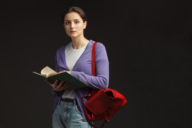 Attractive female student stand with red backpack and leafing education book isolated