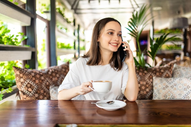 カフェで休憩しながら携帯電話で会話をするかわいい笑顔の魅力的な女性