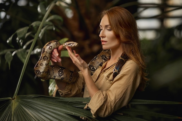 Привлекательная женщина-смотритель зоопарка со змеей питон в тропической природе