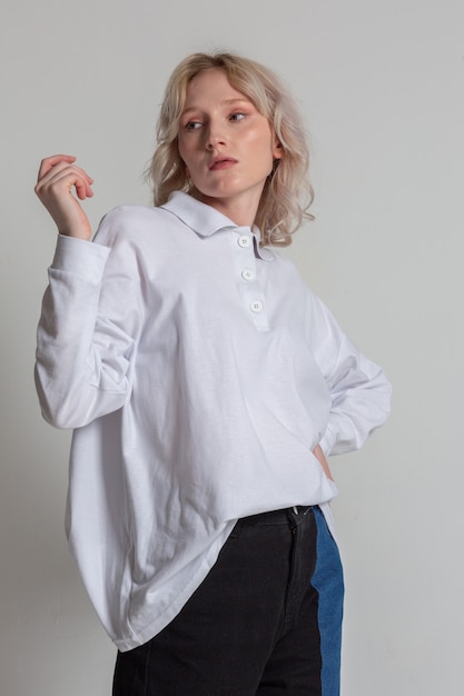 Attractive and feminine blond young woman in a white shirt posing on the white background