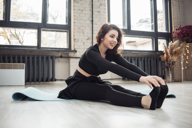 Attractive fit brunette woman practicing stretching on mat indoors