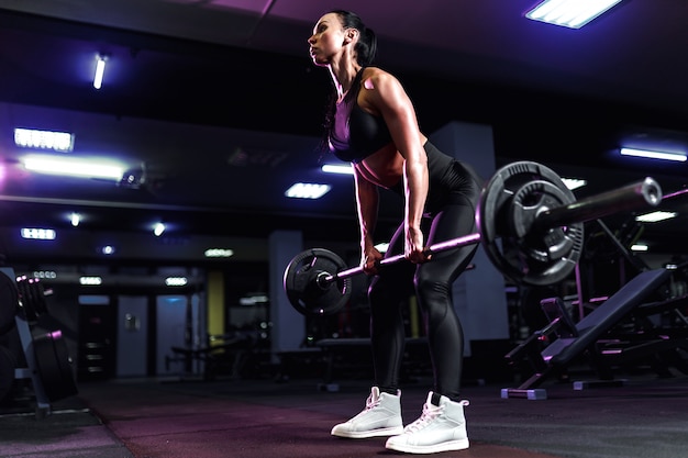 Attractive fit sexy woman in the gym crouches with a barbell. Woman training back