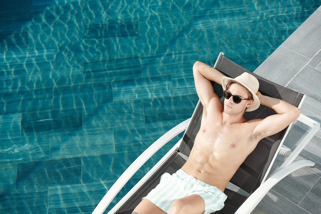 Attractive fit young man resting on chaise-lounge on summer day