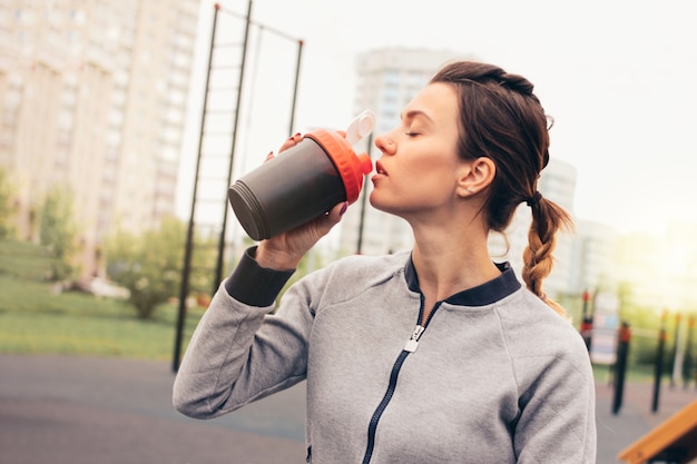 Attractive fit young woman in sport wear drink water and rest on street workout area.