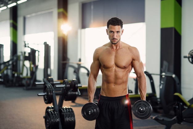 Привлекательный фитнес человек работает с гантелями во время тренировки бицепса в тренажерном зале. Спортивная и здоровая концепция.