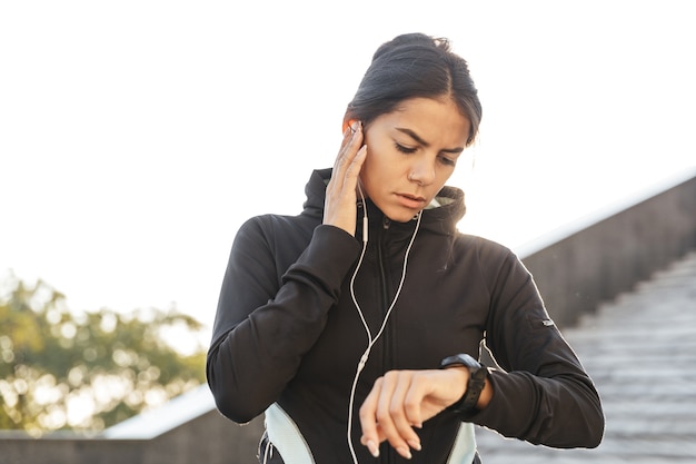 屋外で運動し、イヤホンで音楽を聴いてスポーツウェアを着ている魅力的なフィットネス女性