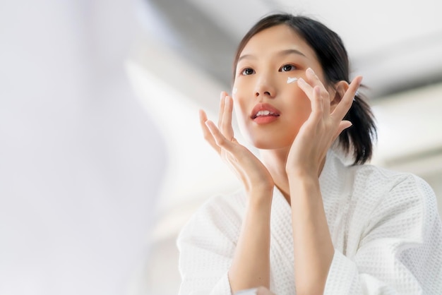 Привлекательная свежесть азиатская женщина чистит лицо пресной водой с осторожностью смотрит в зеркало на домашнем фоне ванной