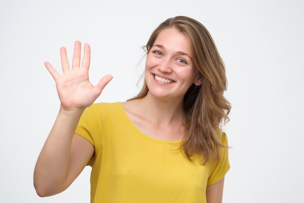 Attractive friendly looking young woman smiling happily, showing five fingers.