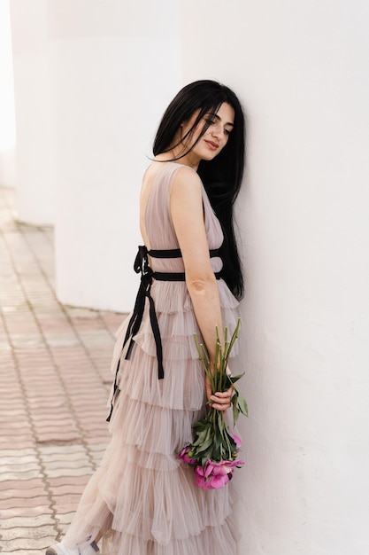 Attraente donna georgiana con peonie bouquet di fiori è in posa in città modello attraente in abito moda con fiori stile di vita