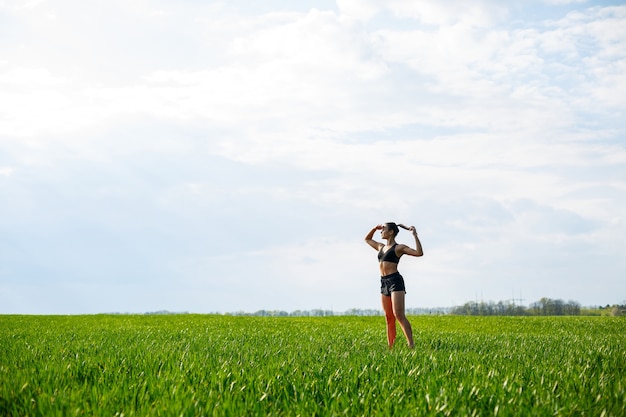 Attractive girl athlete does warm-up outdoors, exercises for muscles. Young woman go in for sports, healthy lifestyle, athletic body. She is in sportswear, black top and shorts