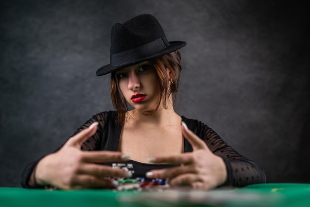 Photo attractive girl in a black dress is leaning on the table holding a poker chip and looking away poker casino