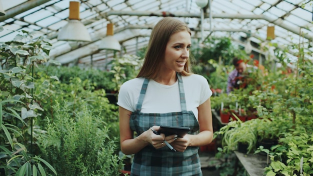 Attractive girl check and count flowers using tablet computer during work in greenhouse