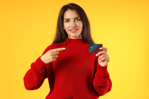 Attractive girl holds credit card on yellow background.