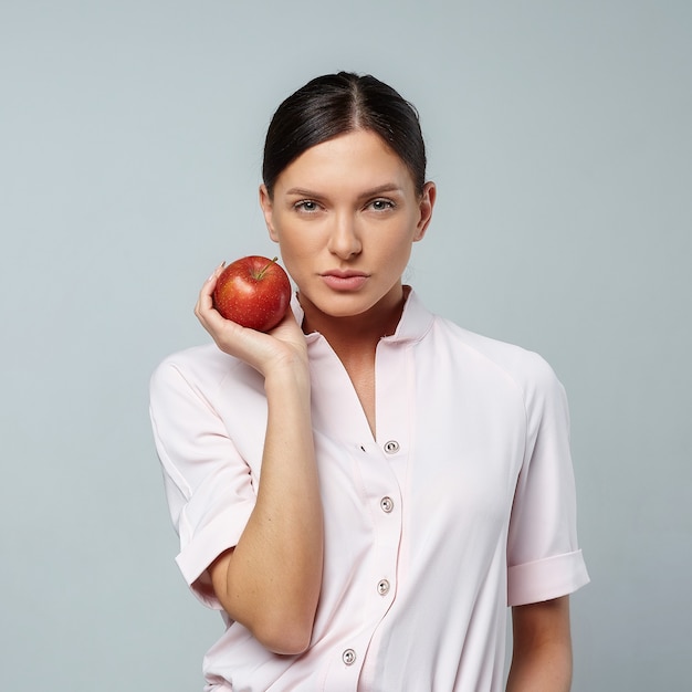 An attractive girl holds a red Apple in her hand in front of her face