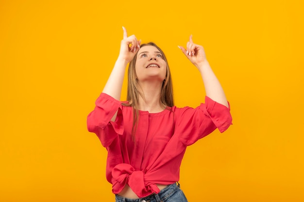 Attractive girl looks up in surprise and points her fingers at something young woman pointing to copy space