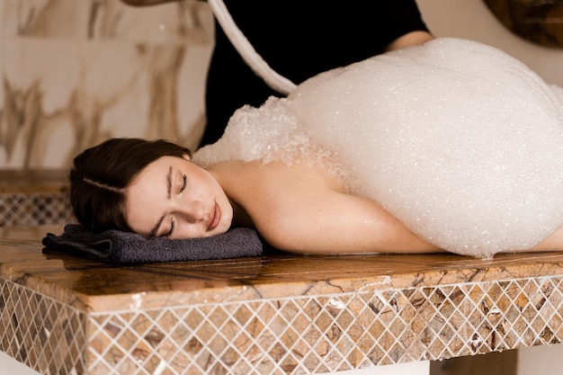 Attractive girl relaxing in spa Masseur is making foam peeling in Turkish spa hammam