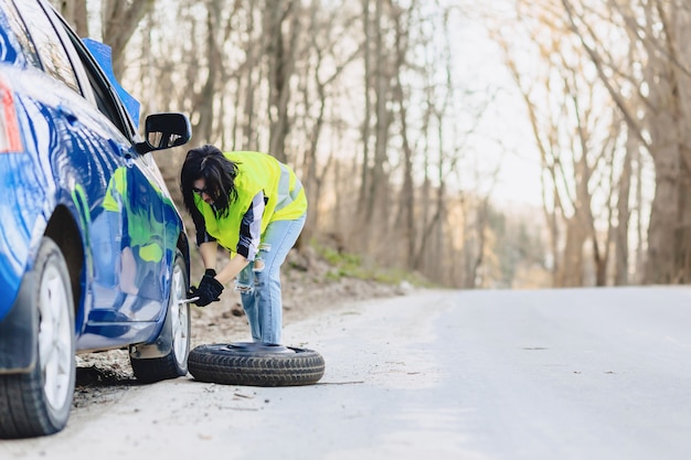 Attractive girl remove wheel from car at road alone