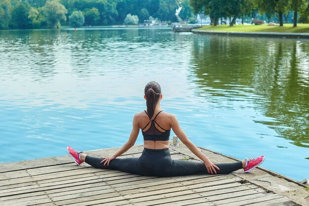 Foto attraente ragazza in abiti sportivi fa esercizi ginnici su un molo in legno in un parco cittadino.