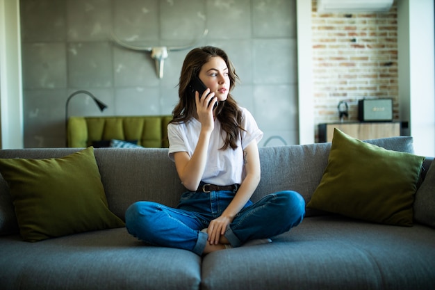 Attractive girl talking on the phone sitting in the sofa at home