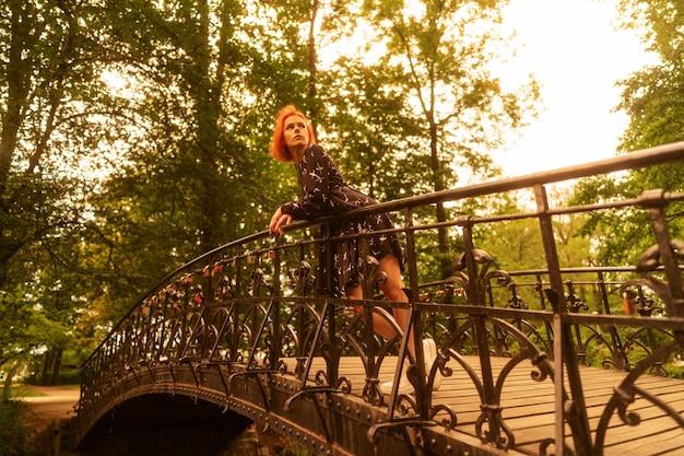 Attractive girl walks alone on the bridge over the river in the park under sunny sky as wallpaper