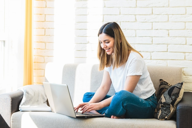 La ragazza attraente con il bello sorriso a casa facendo uso del suo computer portatile per la distanza impara