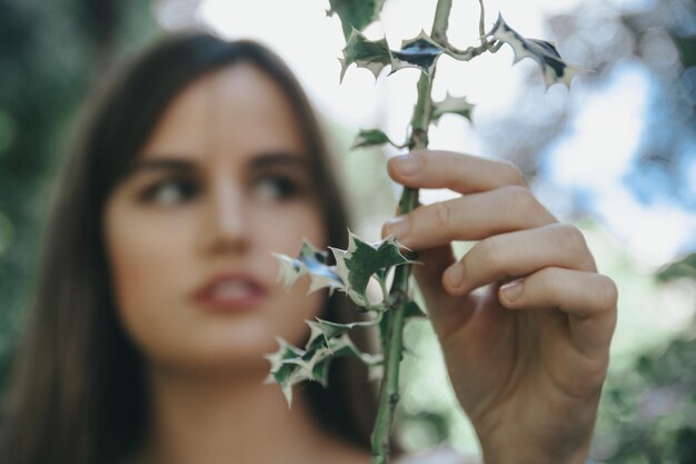 Foto ragazza attraente con capelli lunghi marroni che posano davanti agli alberi verdi mentre toccano i rami