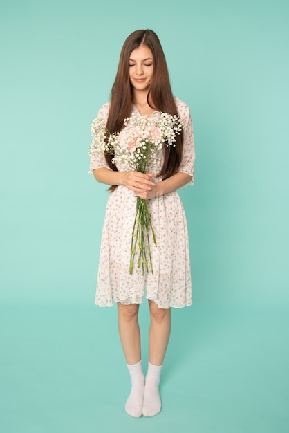 Attractive girl with long brunette hair wearing spring dress, holds white flowers in hands