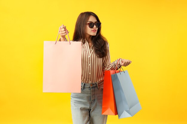 Attractive girl with multicolored paper bags on yellow background.