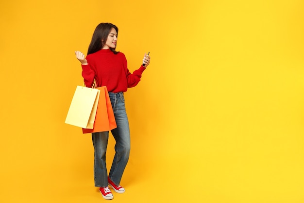 Attractive girl with paper bags and smartphone on yellow background.