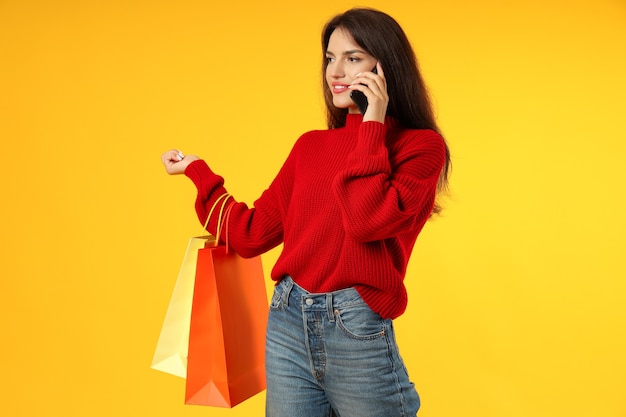 Attractive girl with paper bags and smartphone on yellow background.