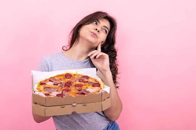 Привлекательная девушка с пиццей в коробке для доставки на розовом фоне.