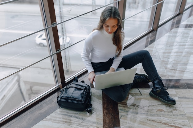 ノートパソコンと空港ターミナルや床のオフィスで物事を扱う魅力的な女の子。旅行の雰囲気または代替の仕事の雰囲気。