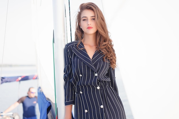 Attractive girl on a yacht at summer day. Close up of fashion portrait of stunning romantic woman posing yacht. Wearing an elegant dress, summer outfit. Blue sky. sunset