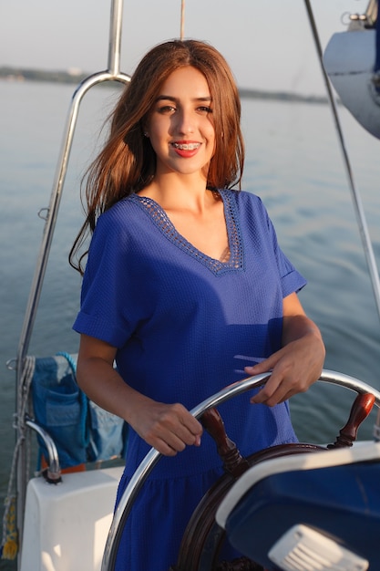 Attractive girl on a yacht at summer day. Close up of fashion portrait of stunning romantic woman posing yacht. Wearing an elegant dress, summer outfit. Blue sky. sunset
