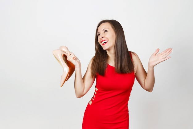 Giovane donna sorridente alla moda caucasica felice glamour attraente in abito rosso che ottiene scarpe beige con suola rossa del suo shopping isolato su priorità bassa bianca. copia spazio per la pubblicità.