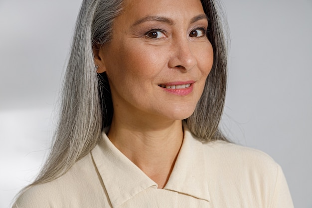 Attractive grey haired mature lady in stylish shirt smiles to camera in studio