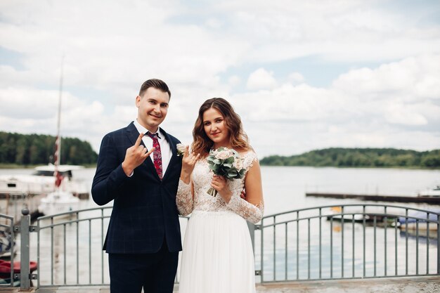 Sposo attraente in abito nero con la sua bella sposa in abito bianco lungo vicino al lago