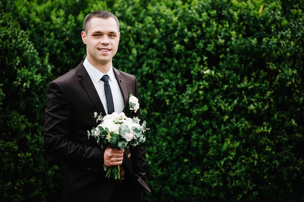 Lo sposo attraente in giacca e cravatta con bouquet di fiori e un fiore all'occhiello o un'asola sulla giacca.