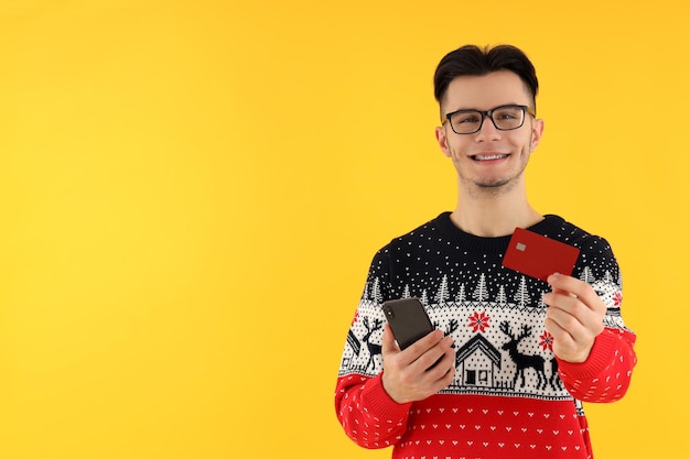 Attractive guy with credit card and phone on yellow background