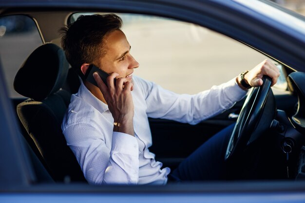 Attractive handsome businessman talking with phone while driving a car in the city