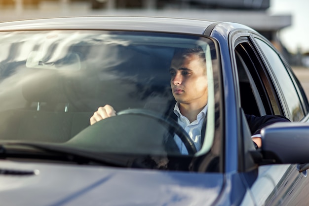 Uomo elegante bello attraente in un vestito alla guida di un'auto costosa