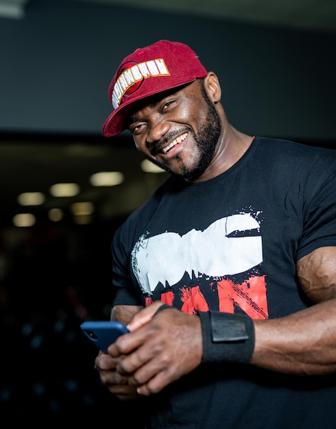 Attractive handsome man in cap smilling in gym. Muscular strong male resting in the gym.