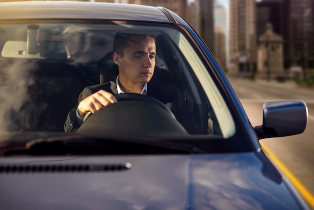 Attractive handsome successful man in white shirt driving an expensive car