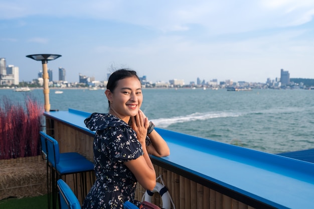 魅力的な幸せなアジアの女性は、夕方、パタヤ市の海辺、タイの街の景色と海に浮かぶテーブルバーに座っています