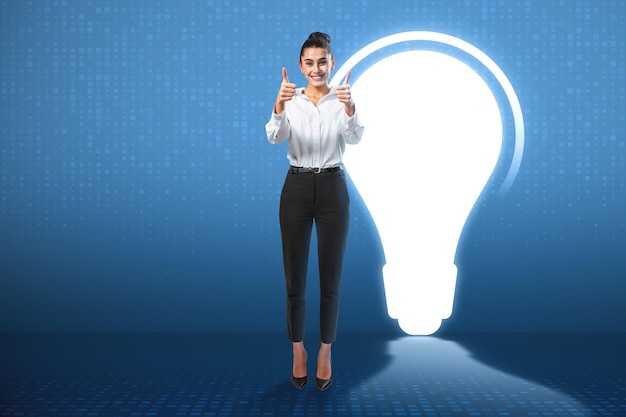 Attractive happy european businesswoman showing thumbs up while\
standing on blue background with abstract glowing light bulb idea\
innovation and success concept