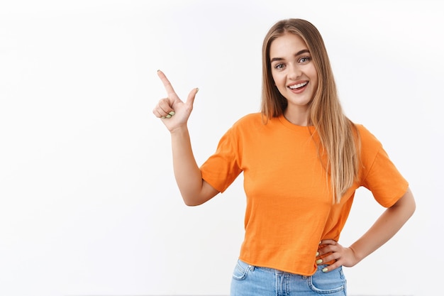 Attractive, happy friendly blonde girl pointing at copy space