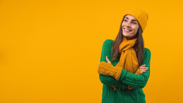 Attractive happy smiling girl wearing warm and cozy sweater hat scarf and mittens posing over orange